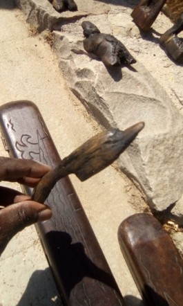 Ibrahima Seydi agafa amb una ma la seva escultura d'un dofí de fusta , Ibrahima Seydi coge con una mano su escultura de un delfin de madera, Ibrahima Seydi takes his wood dolphin sculpture by the hand