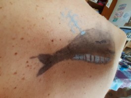  Imatge de Dima i Yana Apareix un fragment d'un colze amb una pintura d'una Balena de color negre que está escopint aigua mentre respira.